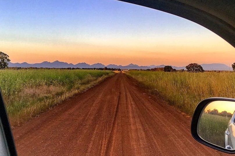 A red dirt road with mountains in the background