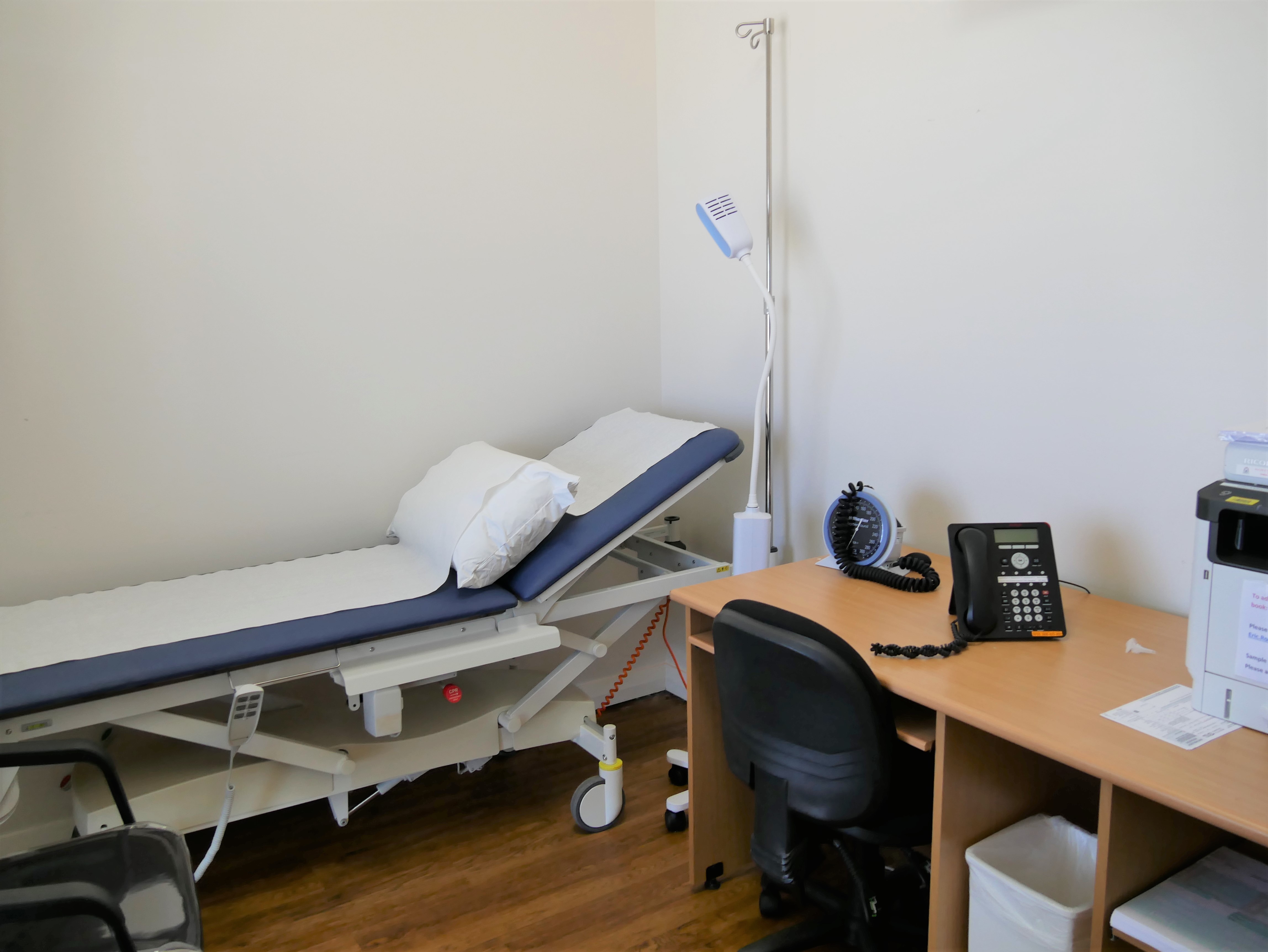 A medical examination bed is next to a desk. 