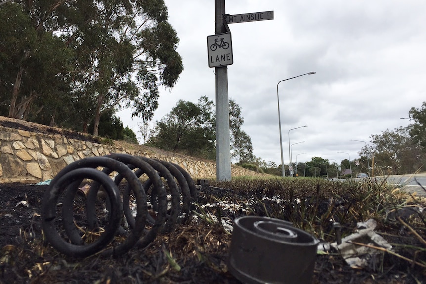 Debris from the car on burnt out grass by the side of the road.