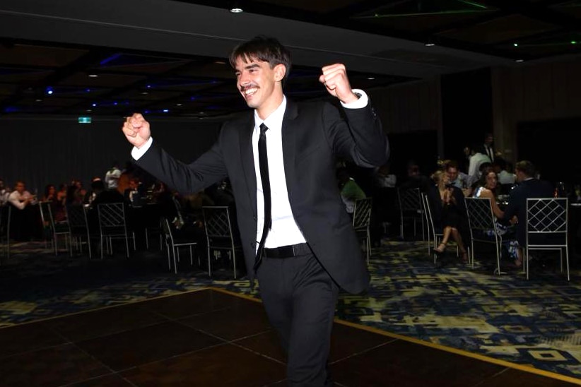 A smiling young man in a suit with his fists in the air at a formal function