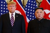 Donald Trump and Kim Jong-un stare stony-faced while standing in front of North Korean and United States flags.