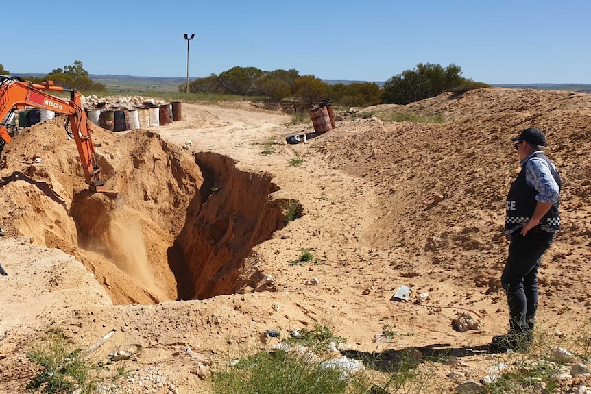 An excavator overseen by police digs a hole during a bikie-related search.