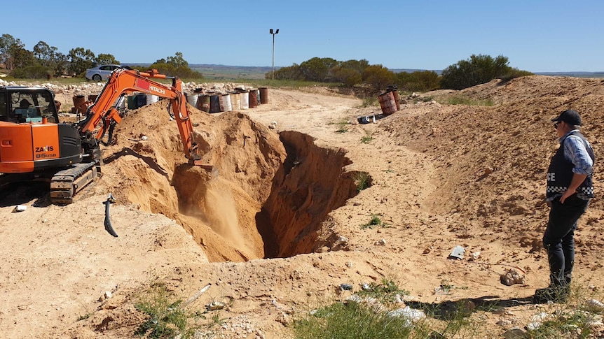 An excavator overseen by police digs a hole during a bikie-related search.