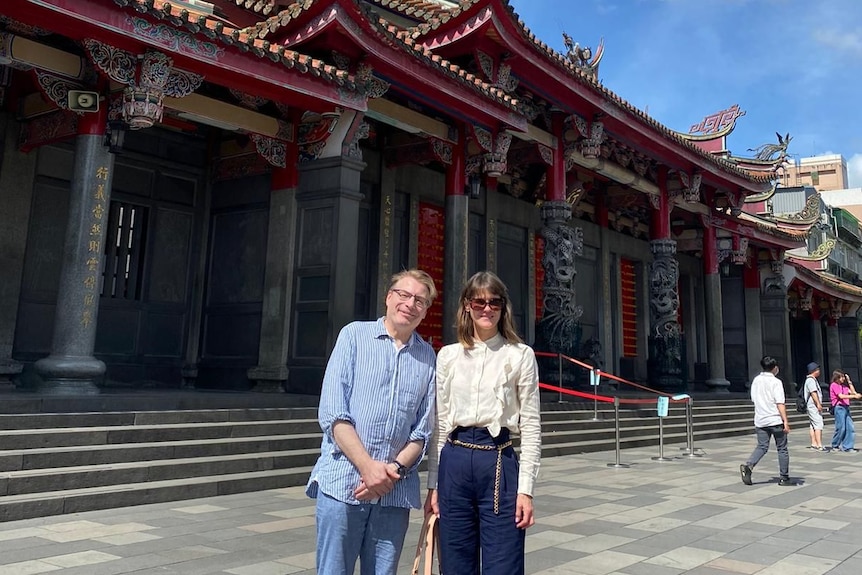 Chris Field in a blue shirt and pants next to Rebecca Poole, in a white shirt and blue pants outside a temple.