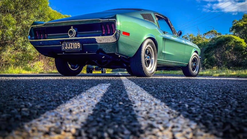 A green Ford Mustang car parked in the middle of the road.