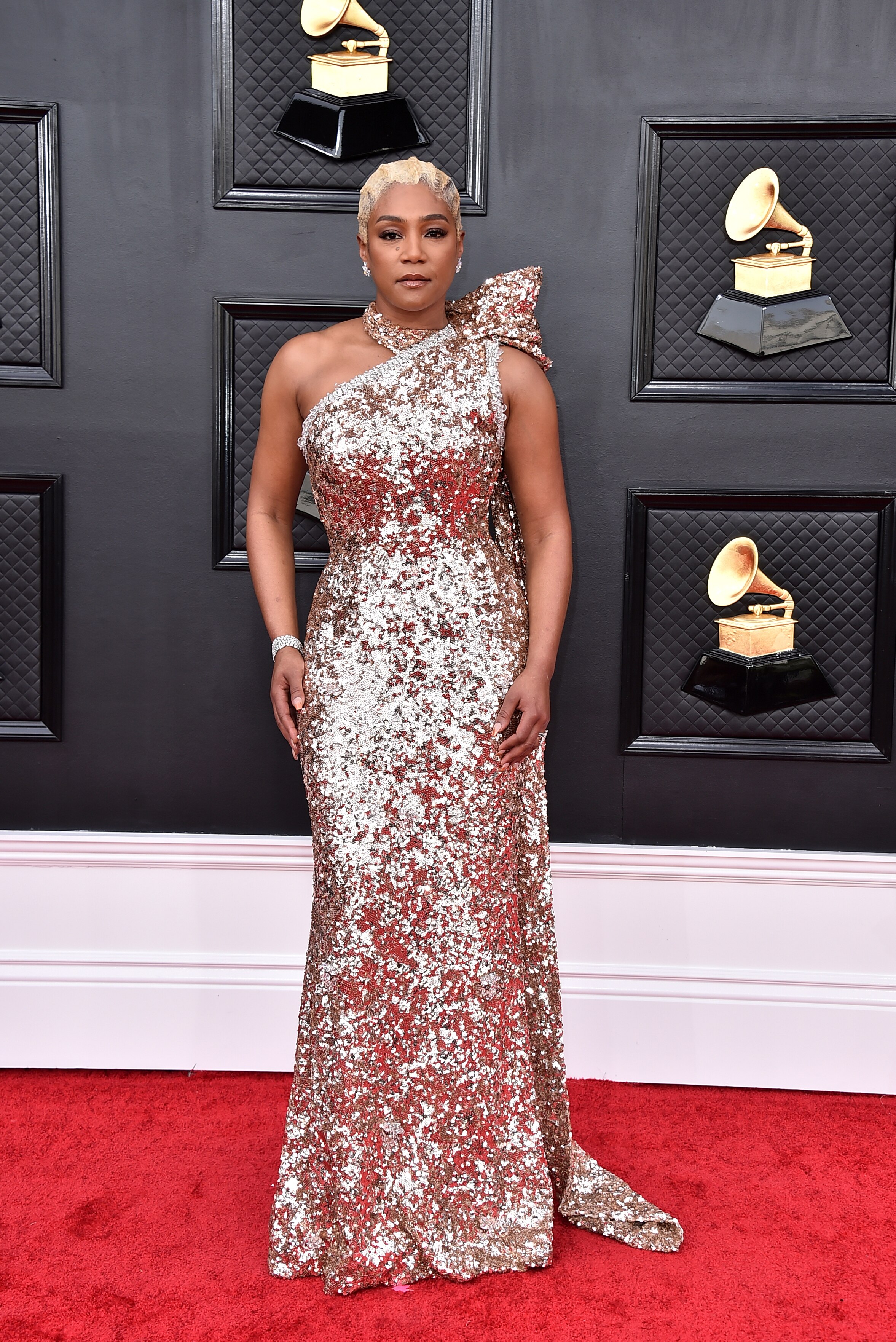 tiffany haddish poses wearing a glittering gold one-shoulder long gown on the grammys red carpet
