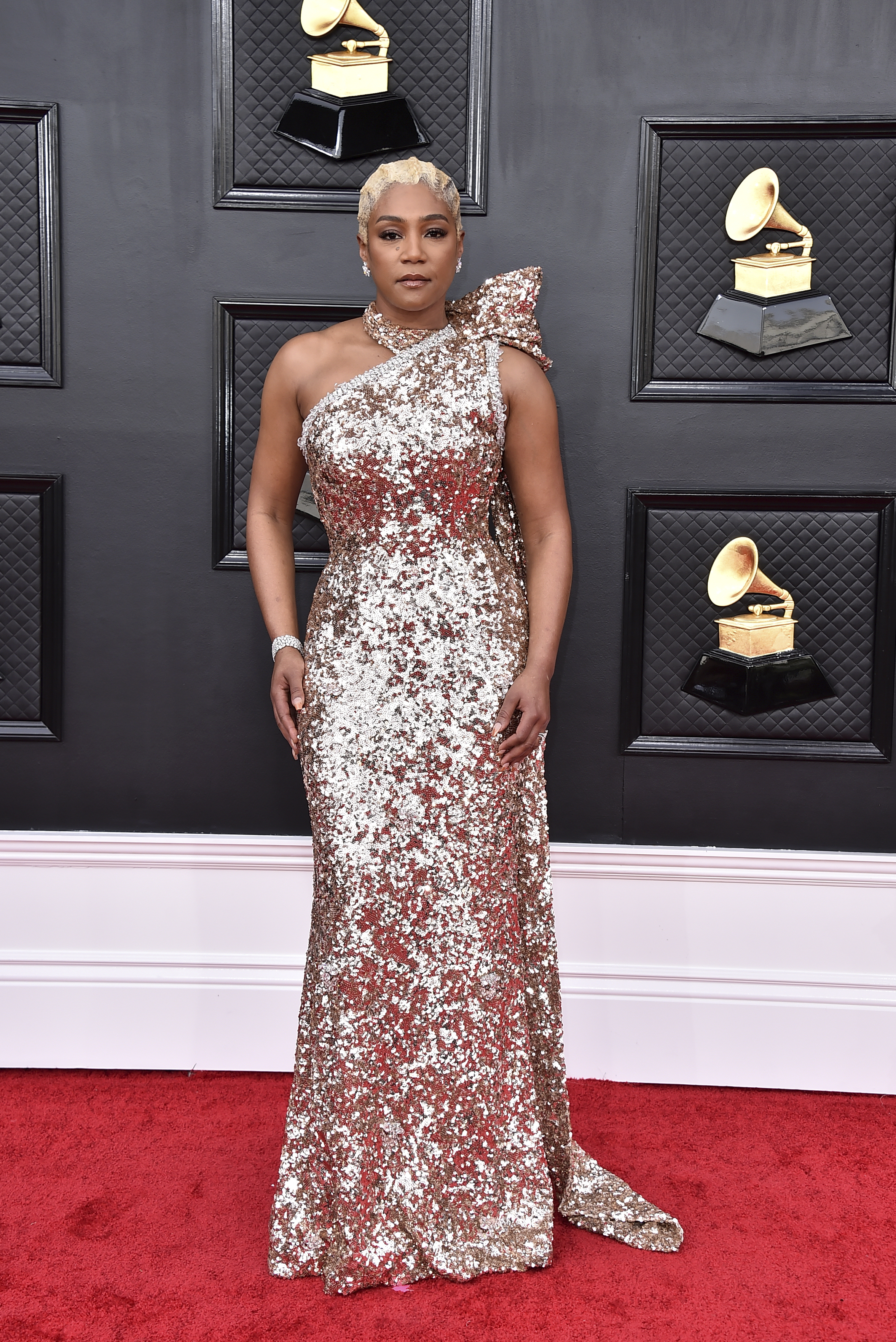 tiffany haddish poses wearing a glittering gold one-shoulder long gown on the grammys red carpet