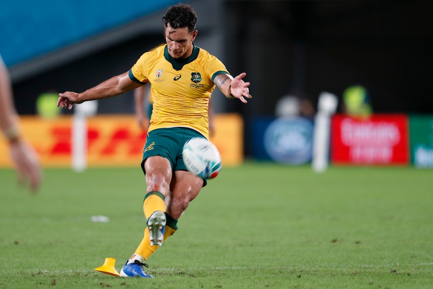 A male rugby union player kicks the ball from a penalty goal attempt with his right foot.