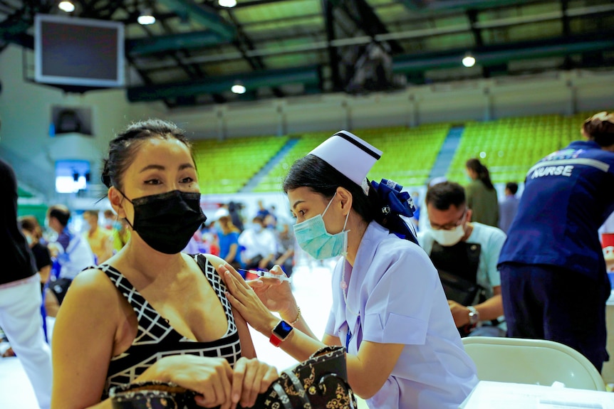 A woman sits in a chair while a nurse holds a needle to her shoulder 