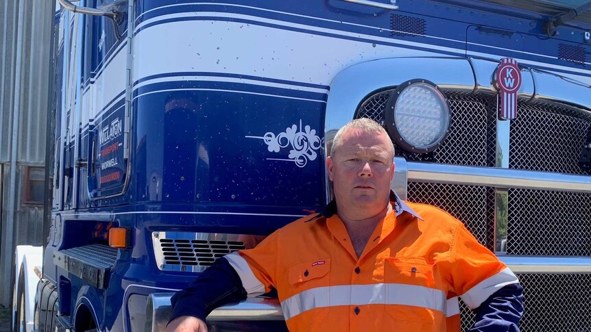 A man in a high-vis orange uniform stands in front of a truck.