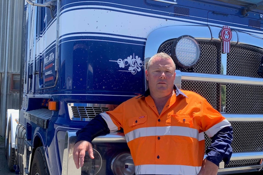 A man in a high-vis orange uniform stands in front of a truck.