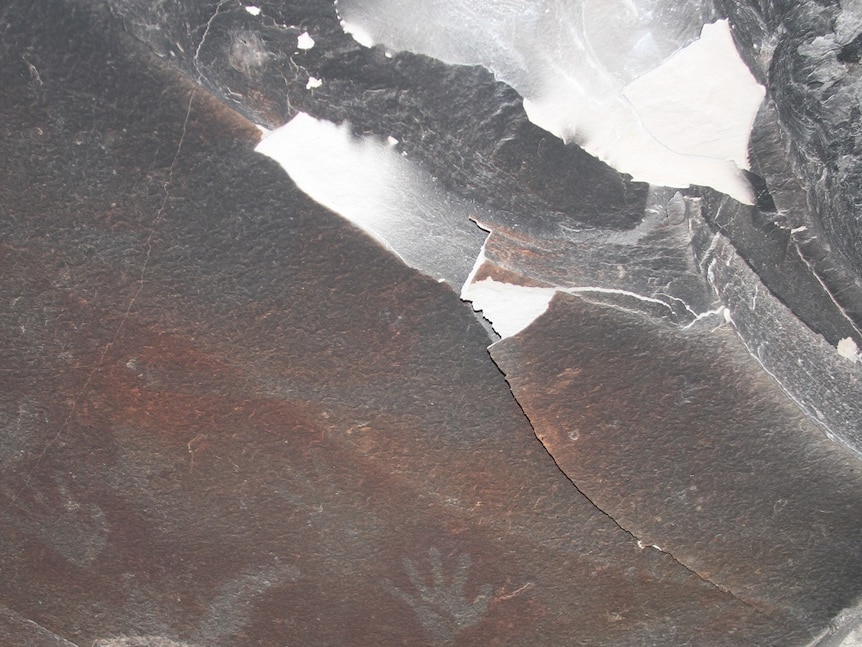 Blackened rock after a fire with some handprints in the rock only slightly visible.