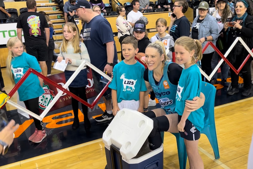Lauren Jackson sits and puts her arms around two young fans while others queue to see her