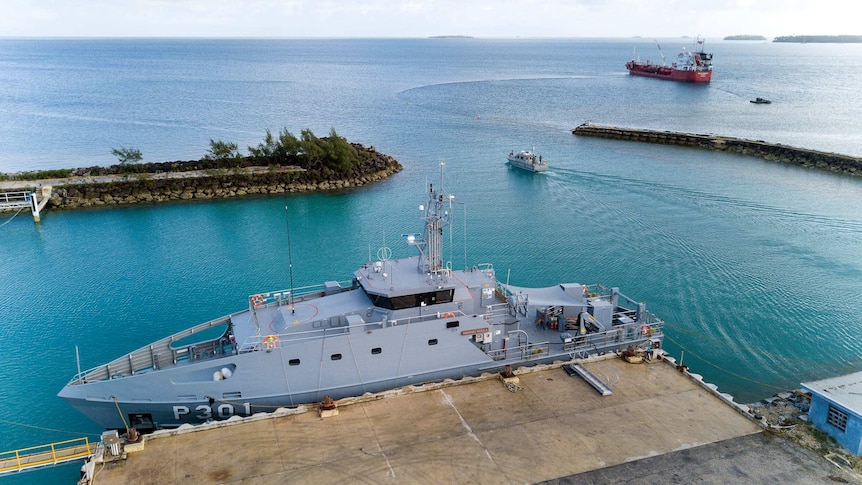 A naval boat is docked beside a wharf with two other boats in the background