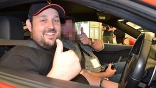 A man in a luxury car giving the thumbs up.