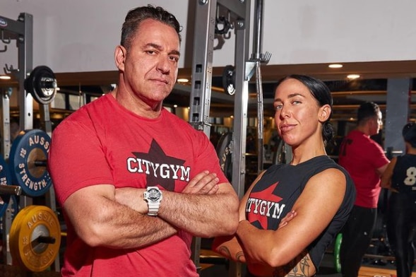 A woman and a man in black and red workout gear with their arms folded, sizing up the camera
