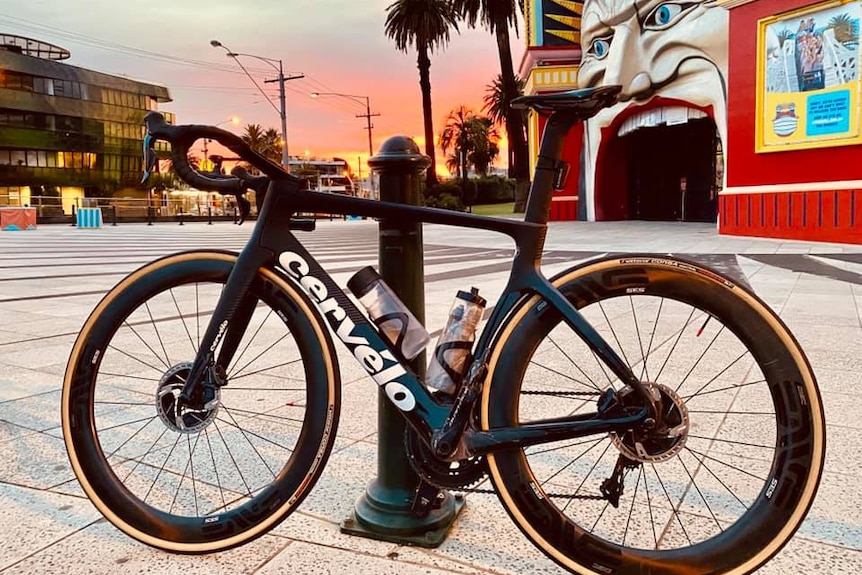 A bicycle rests on a post outside Lunar Park in Melbourne while the sun sets