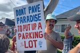 A man holds up a sign that says 'don't pave paradise for a carpark'