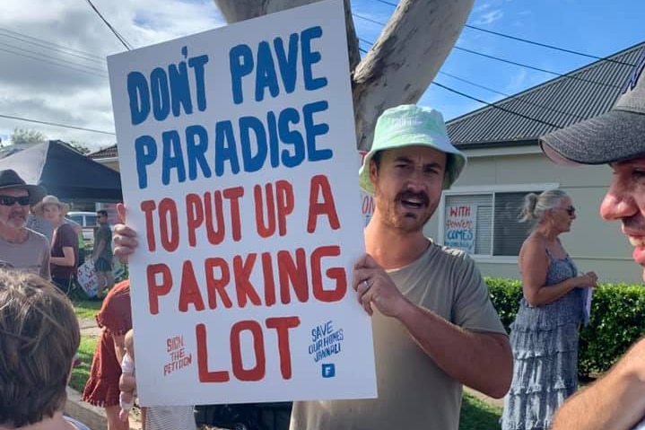 A man holds up a sign that says 'don't pave paradise for a carpark'