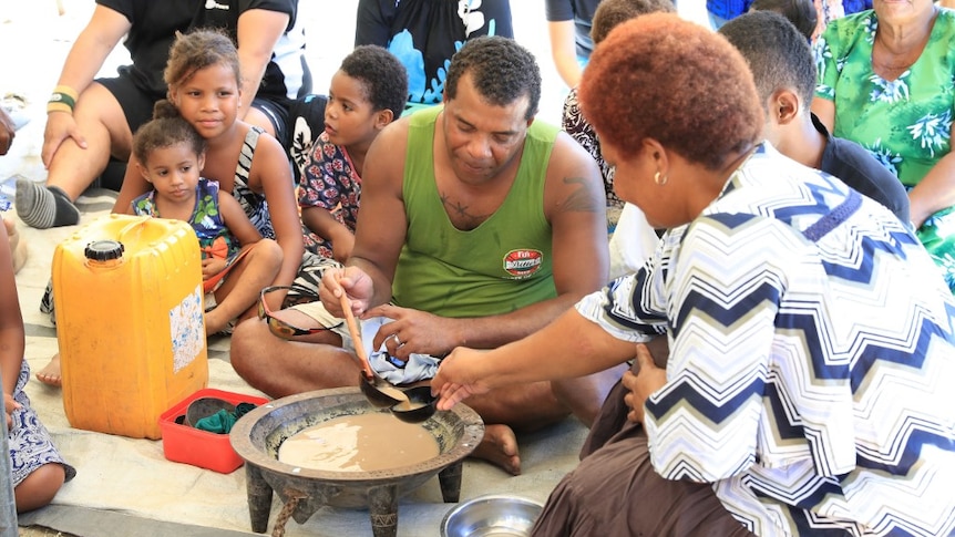 A woman serves kava to rugby player in green singlet.