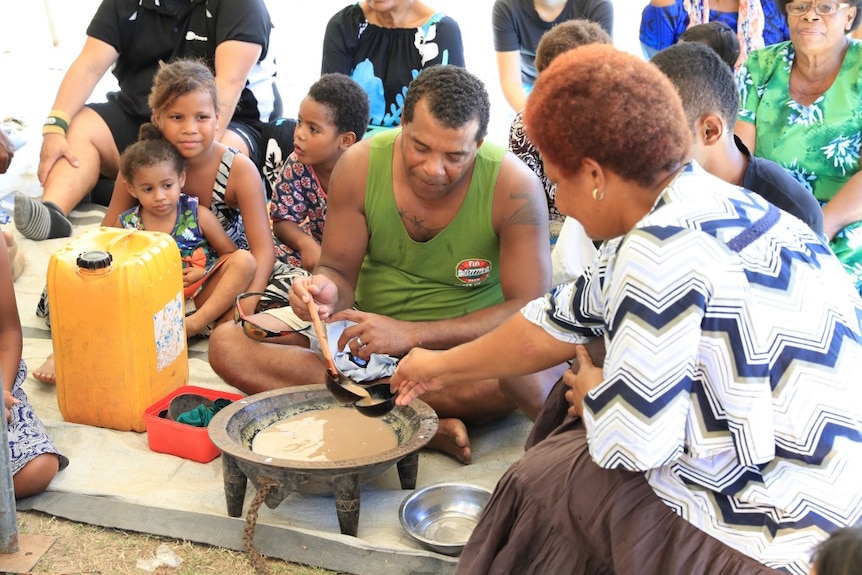 A woman serves kava to rugby player in green singlet.