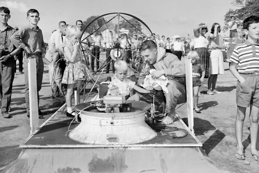A child and onlookers examining a hovercraft.