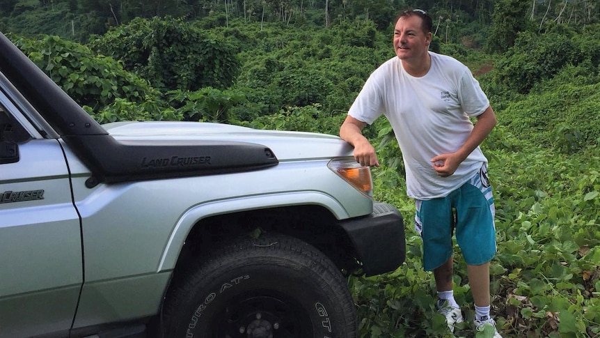 Man standing in jungle clearing and leaning against a four wheel drive.