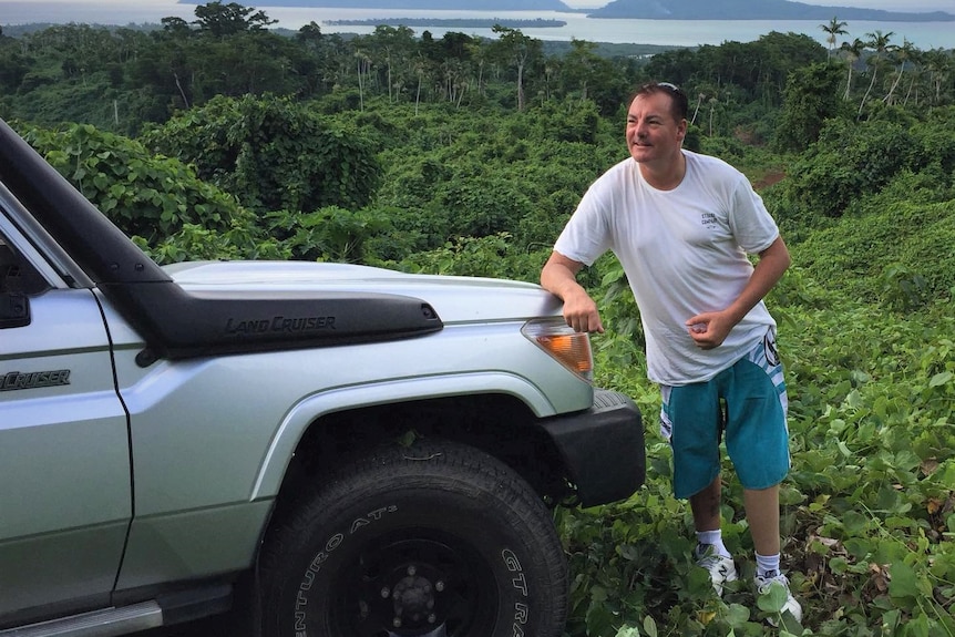 Man standing in jungle clearing and leaning against a four wheel drive.