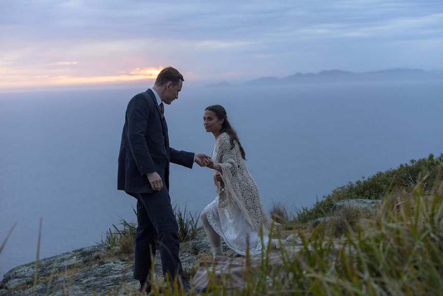 Michael Fassbender and Alicia Vikander on a granite escarpment next to a misty ocean.