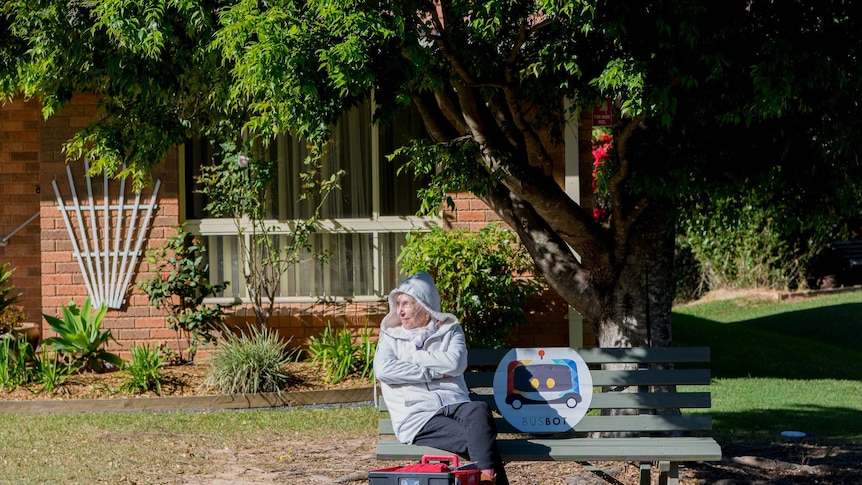 A woman sits at a bus stop.