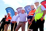 Six men in hard hats with shovels at a sod turning.