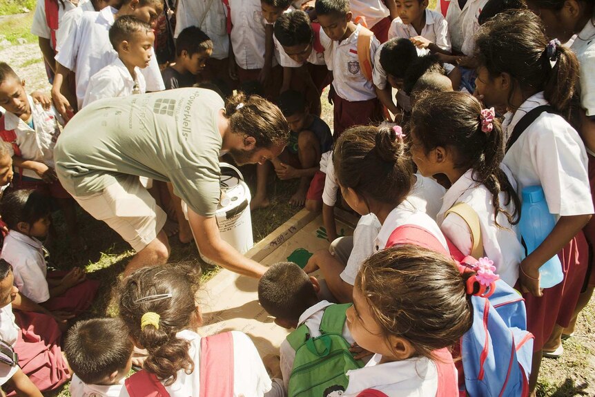School children gather around a man installing a charger in the ground.