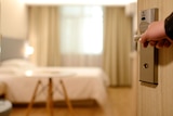 A hand opens the door to a hotel room.