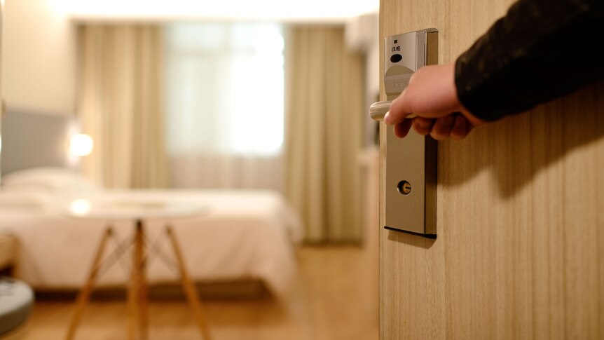 A hand opens the door to a hotel room.