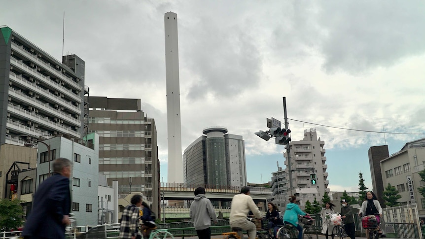 Cyclists cross a road in front of an incineration plant