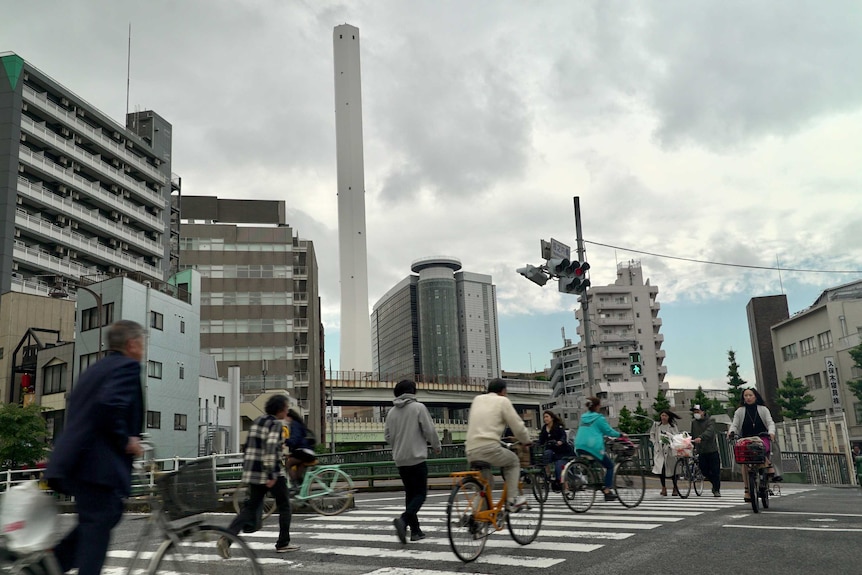 Cyclists cross a road in front of an incineration plant