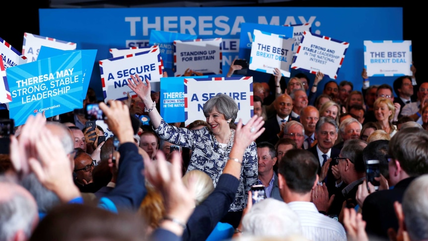 British Prime Minister Theresa May is surrounded by supporters holding up signs at a campaign event.