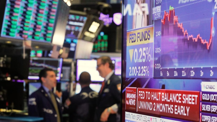 A screen displays the U.S. Federal Reserve interest rates announcement as Wall St traders work