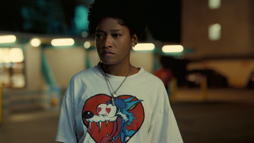 A woman in a white t-shirt featuring a cartoon character stands on the street at night