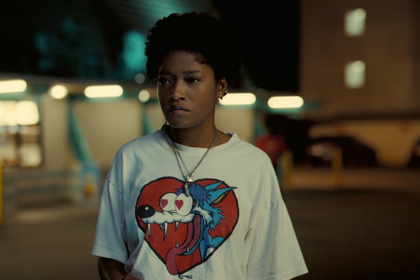 A woman in a white t-shirt featuring a cartoon character stands on the street at night