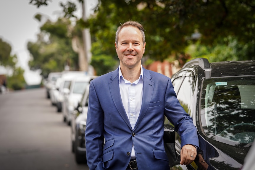 A portrait of a man in a suit, with cars in the background of a street.