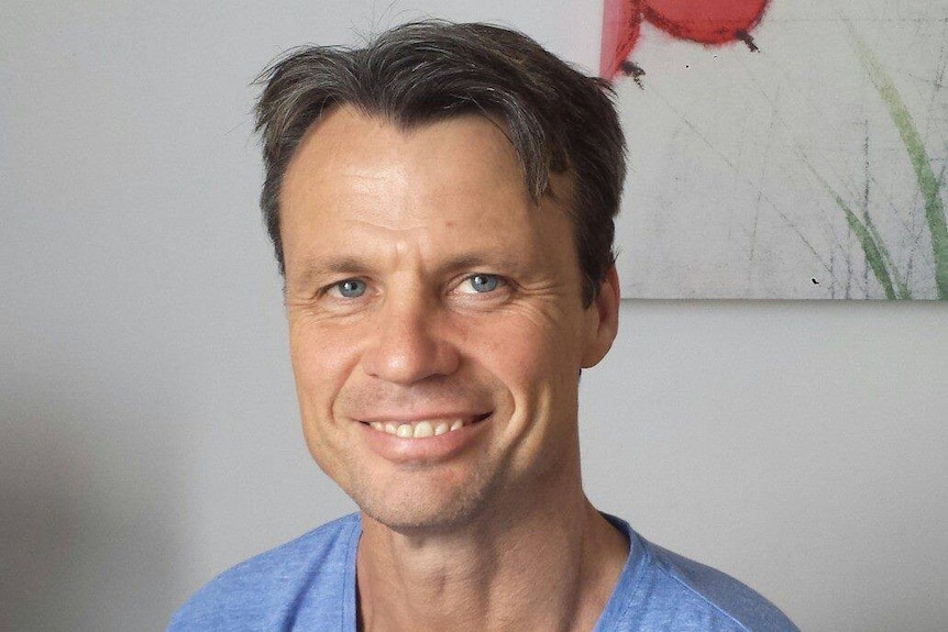 A head shot of a man with short grey brown hair, blue eyes and blue shirt
