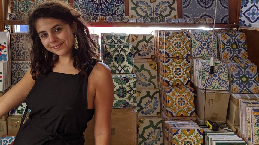 Woman dressed in a black dress stands in front of colourful tiles in a tile shop.