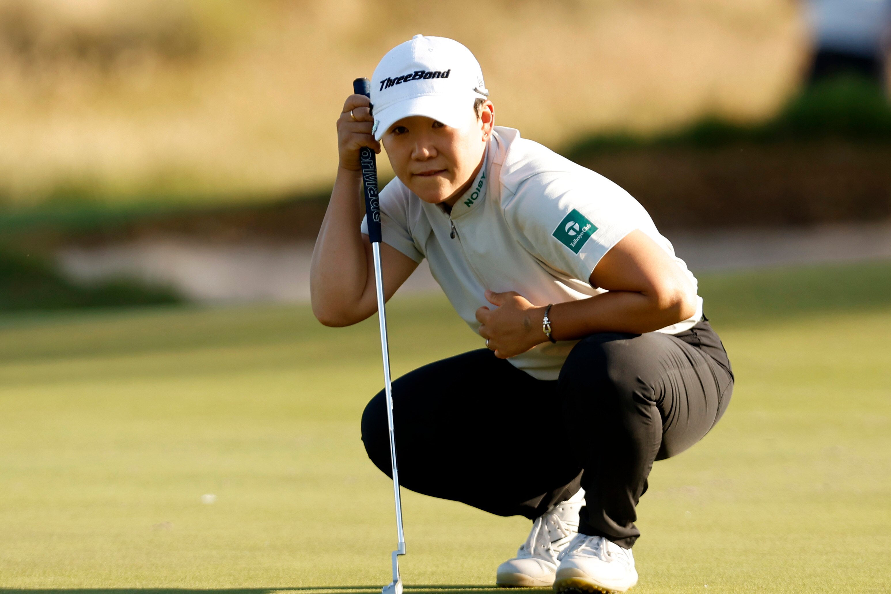 A South Korean female golfer crouches as reads the green ahead of putting at the Australian Open.