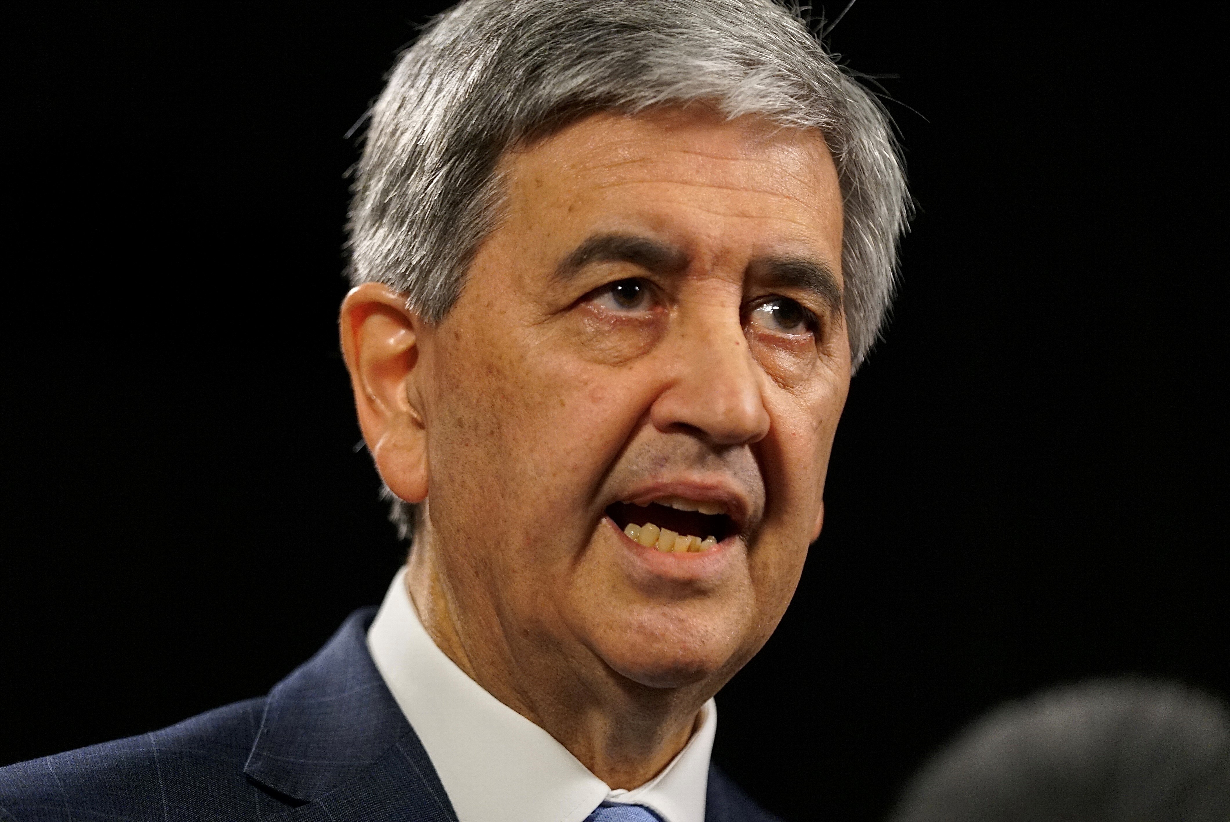 A man wearing a suit and tie speaking with a black background