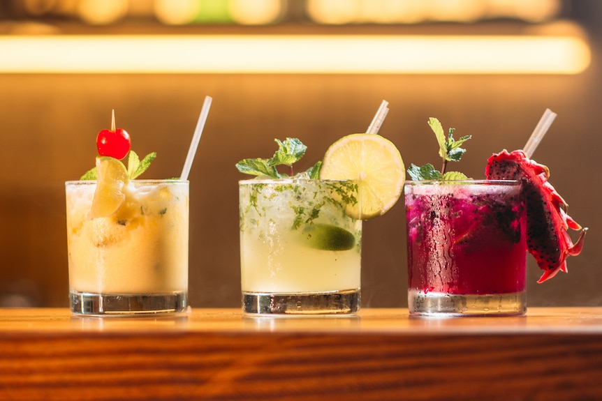 A row of three colourful drinks with garnishes and straws.