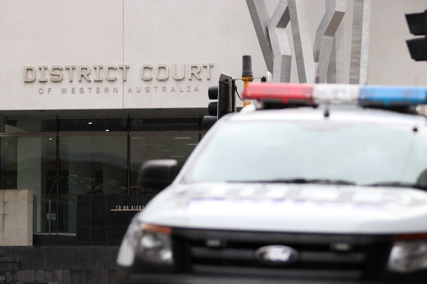A police car blurred in the foreground in front of the District Court in Perth.