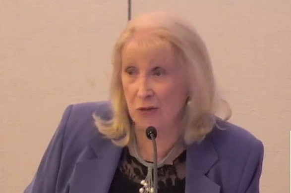 A middle-aged woman with blonde hair and a lilac-coloured jacket speaks in the witness box at a royal commission.