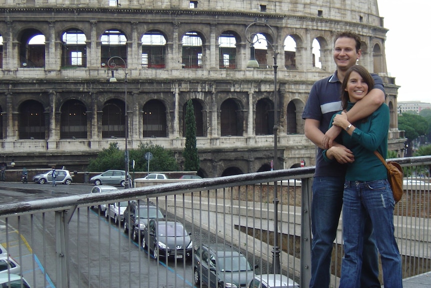 A man and woman stand together in front of colosseum.