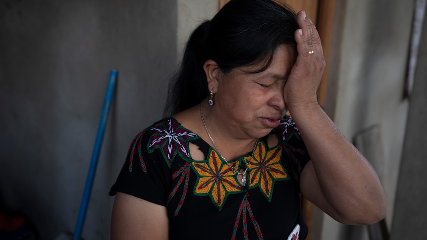 A Guatemalan woman reacts with eyes closed and hand against her forehead.